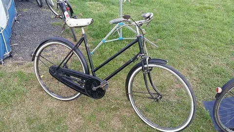 Black ladies' roadster with a full chaincase and white-wall tyres, on a campsite