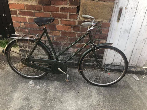 Dark green ladies' bicycle with a rear carrier, leaning against a brick wall