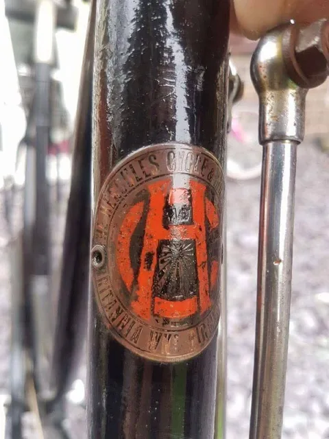 Hercules head badge with an orange H monogram, marked Britannia Wks, Birmingham, on a black frame
