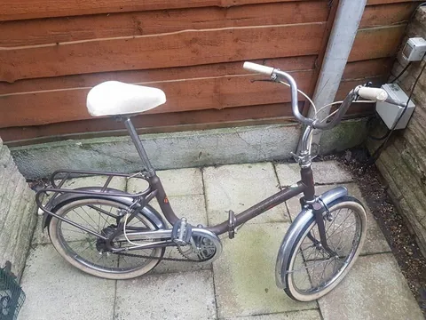 Brown Hercules small-wheel folding bicycle with a white saddle, rear carrier and chrome mudguards