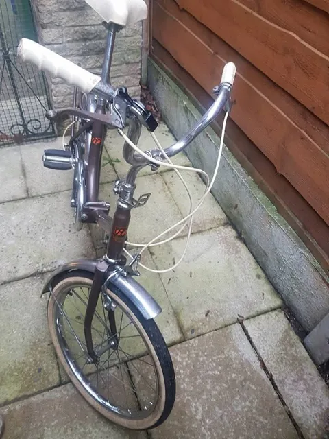 The brown folding bike from the front, with chrome bars and cream cables