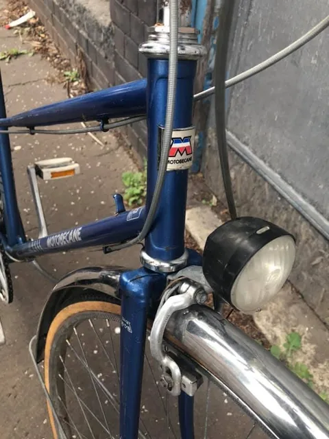 Blue head tube with an M head transfer, a chrome mudguard and a black dynamo headlamp