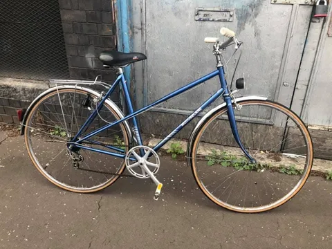 The blue Motobecane from the front three-quarter, with a dynamo headlamp