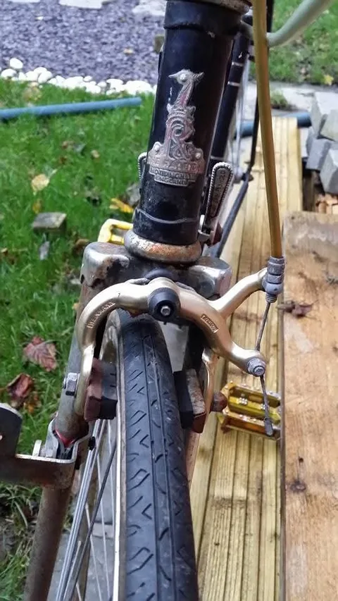 Raleigh heron head badge reading Nottingham England on a black frame, above a gold-coloured calliper brake