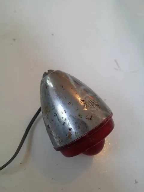 Chrome rear lamp with a red lens, spotted with rust