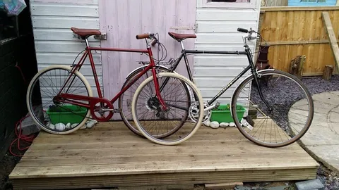 A red bicycle with cream tyres beside a black road bike, on decking