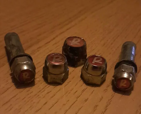 Five Raleigh hub nuts and axle ends with red caps bearing a white R