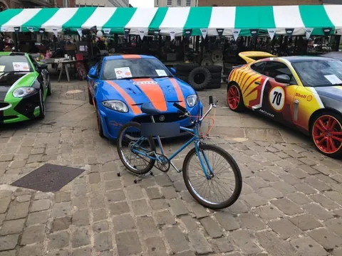 Blue cruiser bicycle with an orange stripe, parked in front of show cars