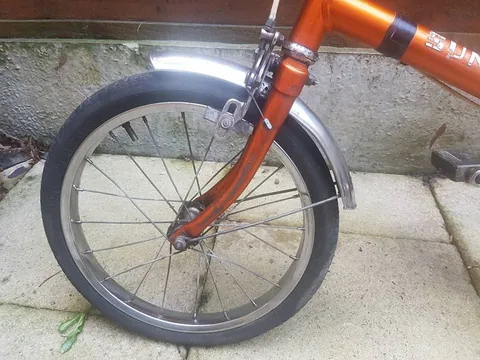 Small front wheel with a calliper brake and chrome mudguard on an orange fork