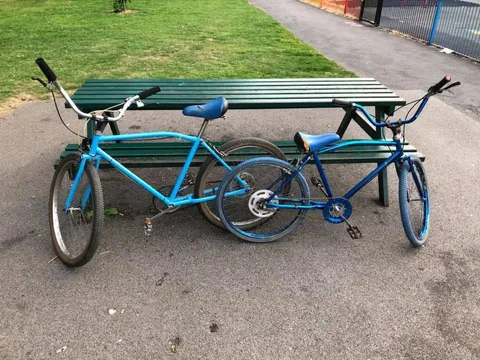 Two blue cruiser bicycles by a picnic bench